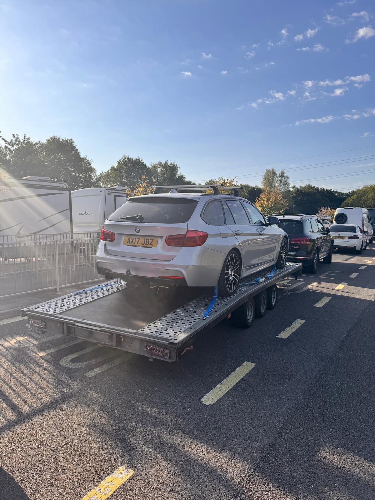 White BMW estate car loaded on a car transporter truck on a highway with other vehicles visible in traffic.