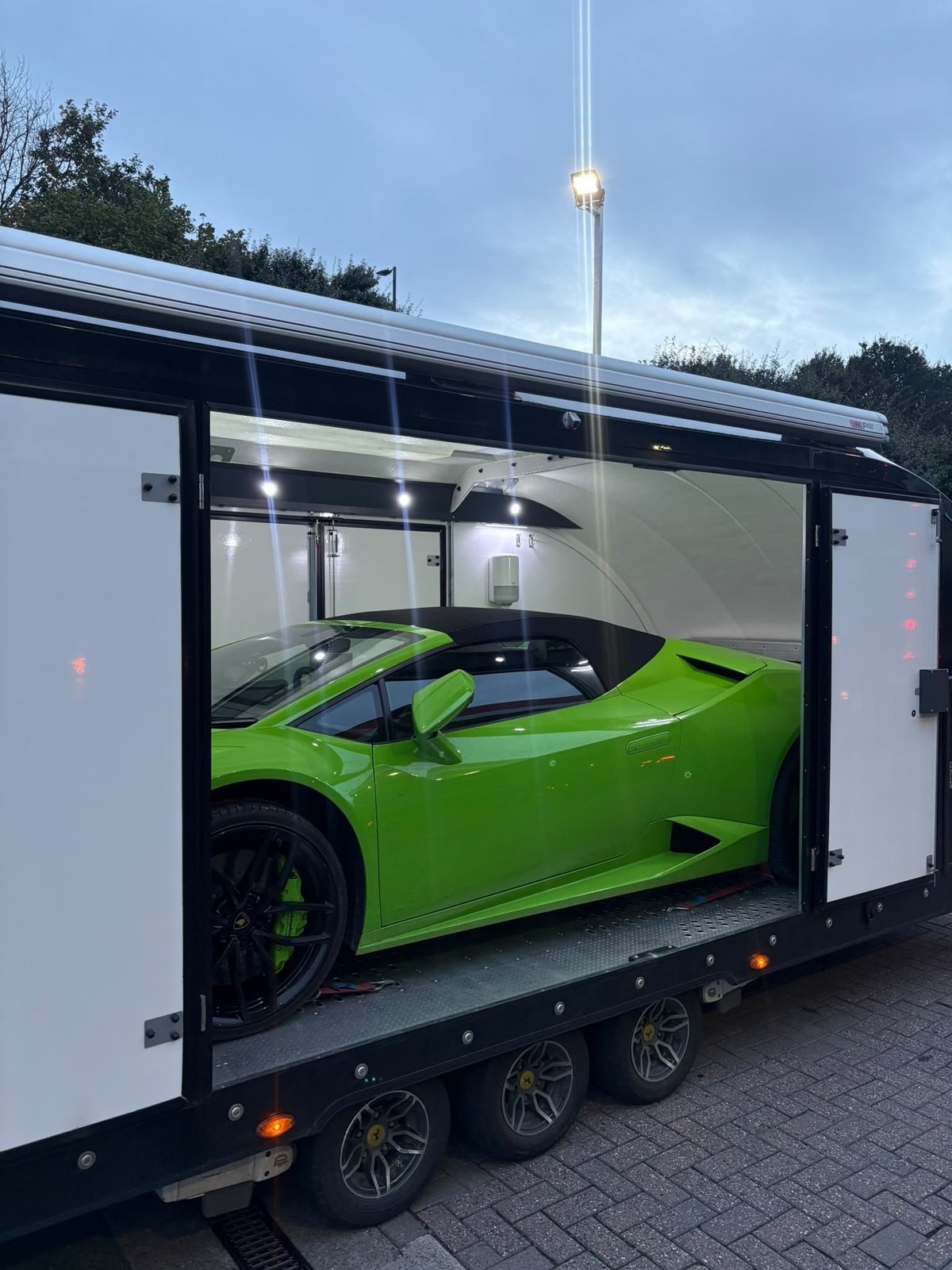 Bright green sports car with black wheels loaded inside a white enclosed car trailer